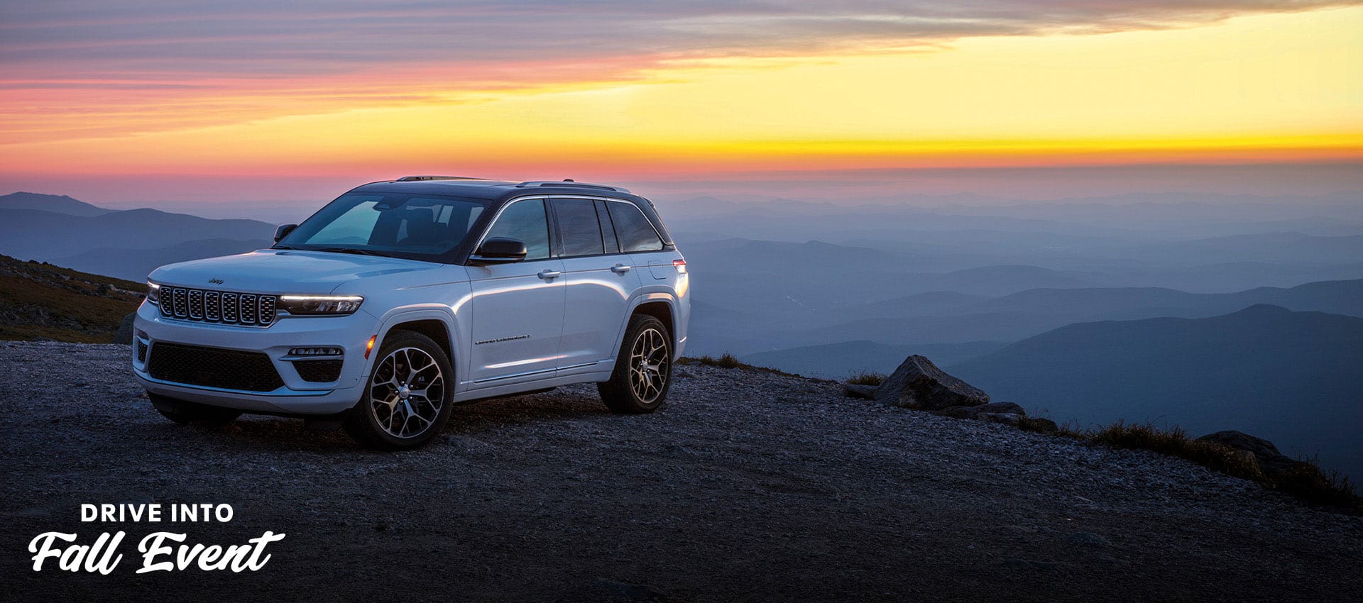 A white 2025 Jeep Grand Cherokee Summit. Reserve parked near the edge of a cliff at sunset. Drive Into Fall Event.