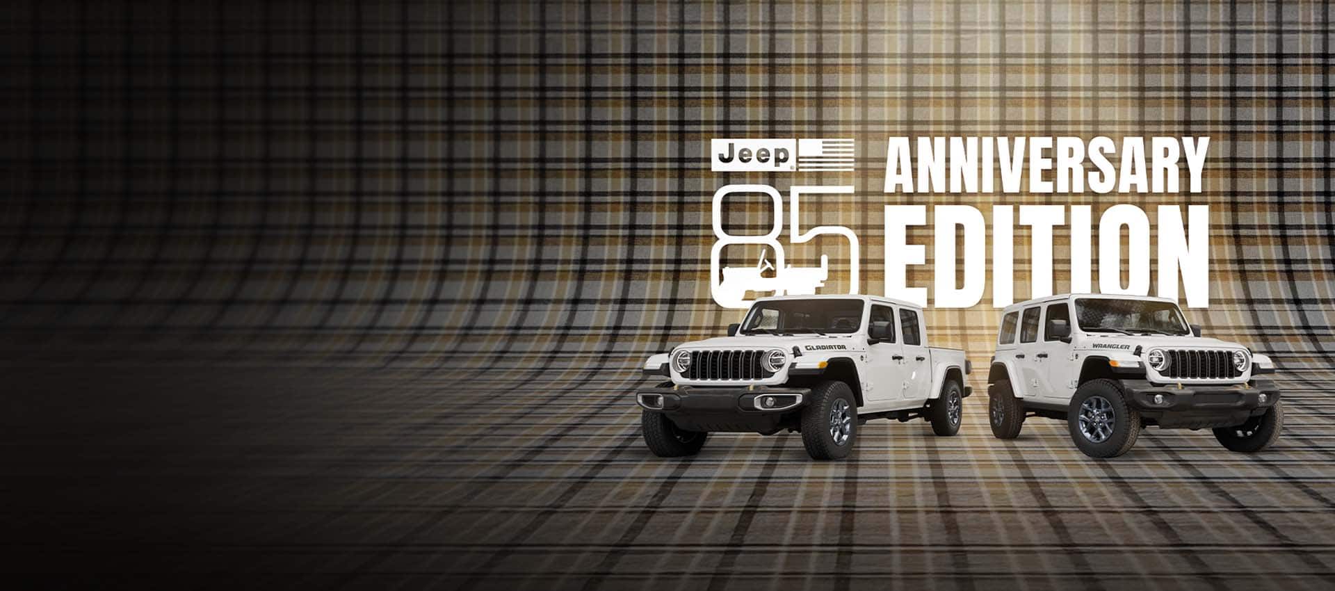 A white 2026 Jeep Gladiator 85th Anniversary Edition on the left and a white 2026 Jeep Wrangler 85th Anniversary Edition on the right, parked on a seamless plaid surface that extends up the wall behind them. Jeep 85 Anniversary Edition.