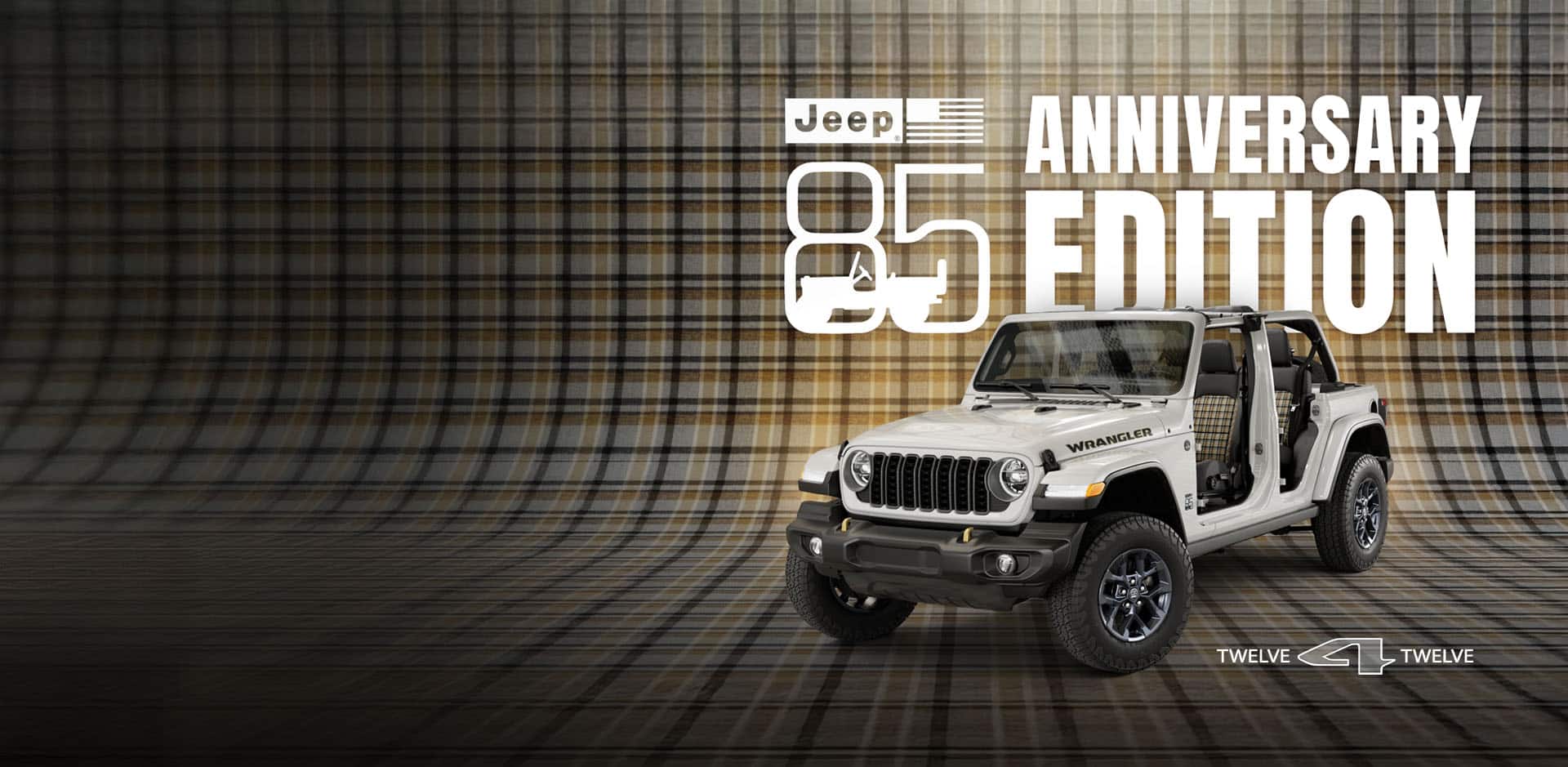 A driver-side front angle of a white 2026 Jeep Wrangler 85th Anniversary Edition with its doors and top removed, revealing plaid inserts on the front and rear seats, parked on a seamless plaid surface that extends up the wall behind it. Jeep 85 Anniversary Edition. 12 for 12.