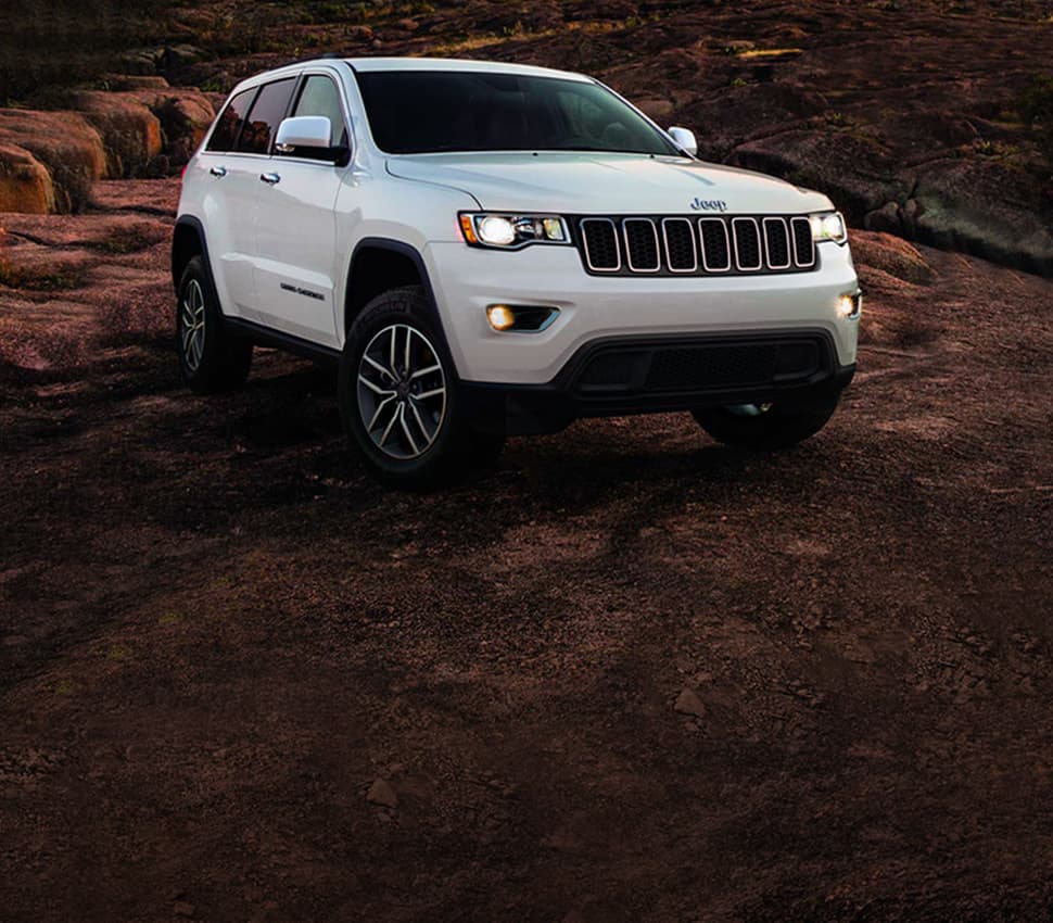 A white 2020 Jeep Grand Cherokee Limited parked off-road in a stony area.