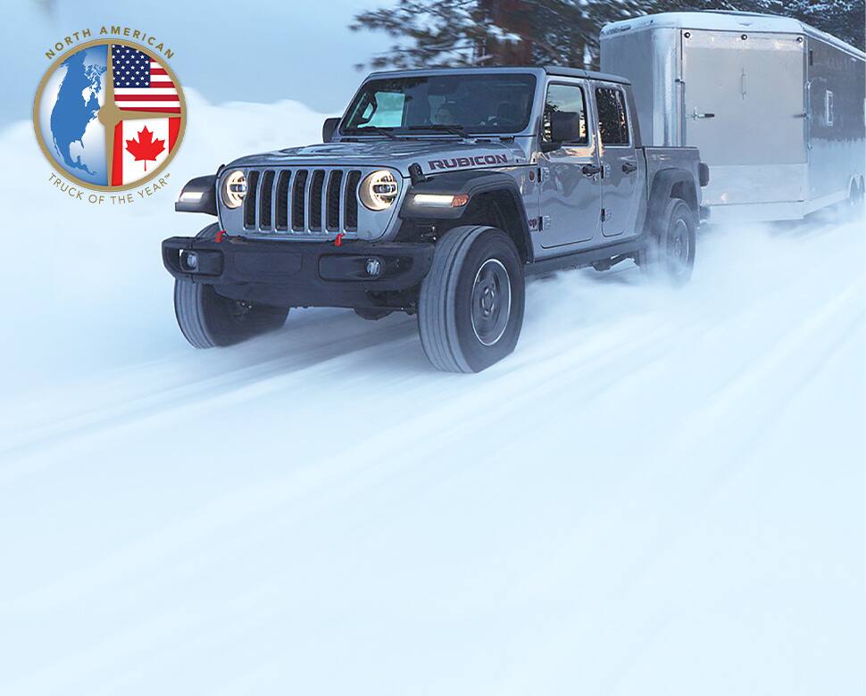 A gray 2020 Jeep Gladiator Rubicon driving on a snow-covered road, towing a camper.