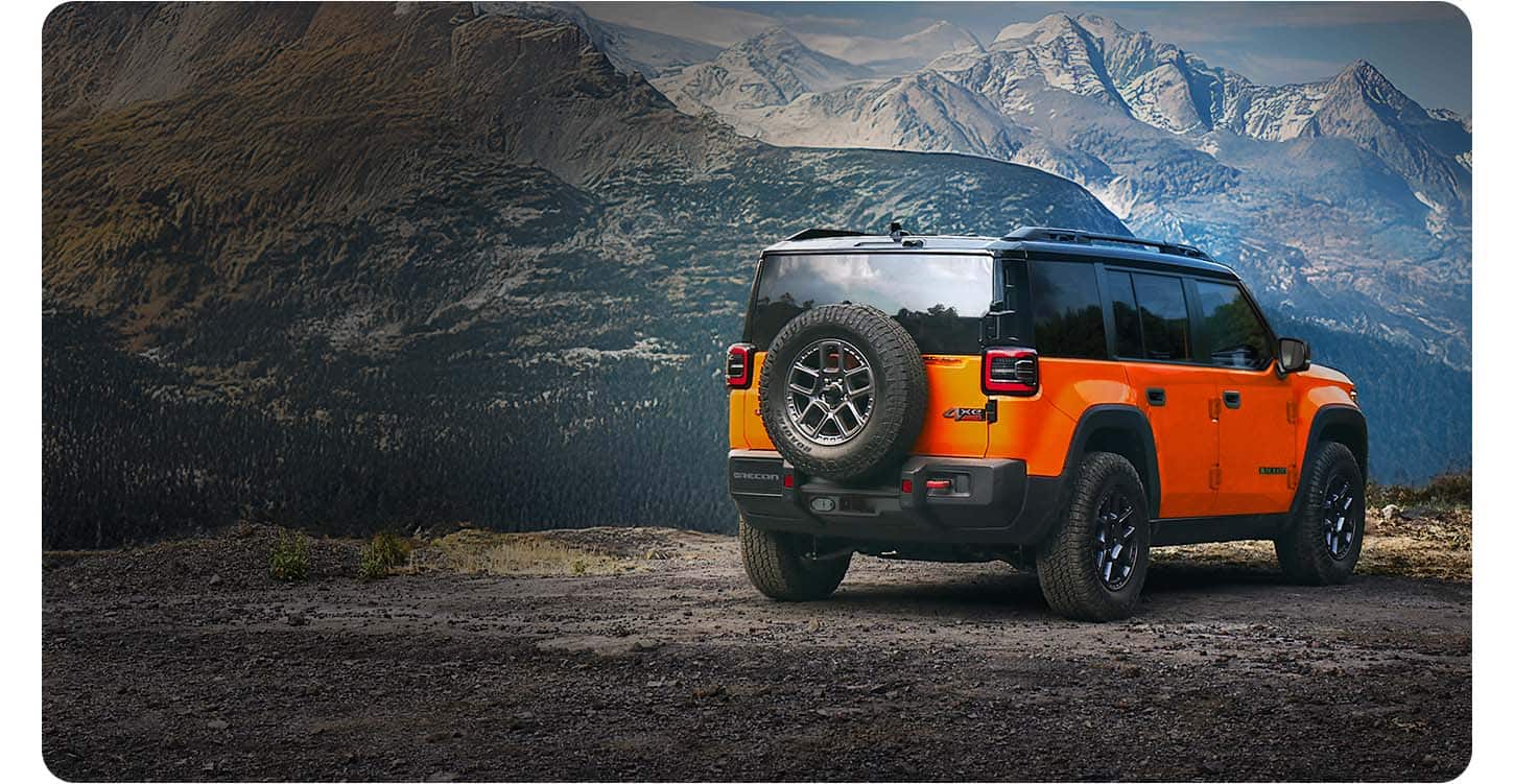 An orange 2026 Jeep Recon Moab with a black roof, parked on a clearing in the mountains.