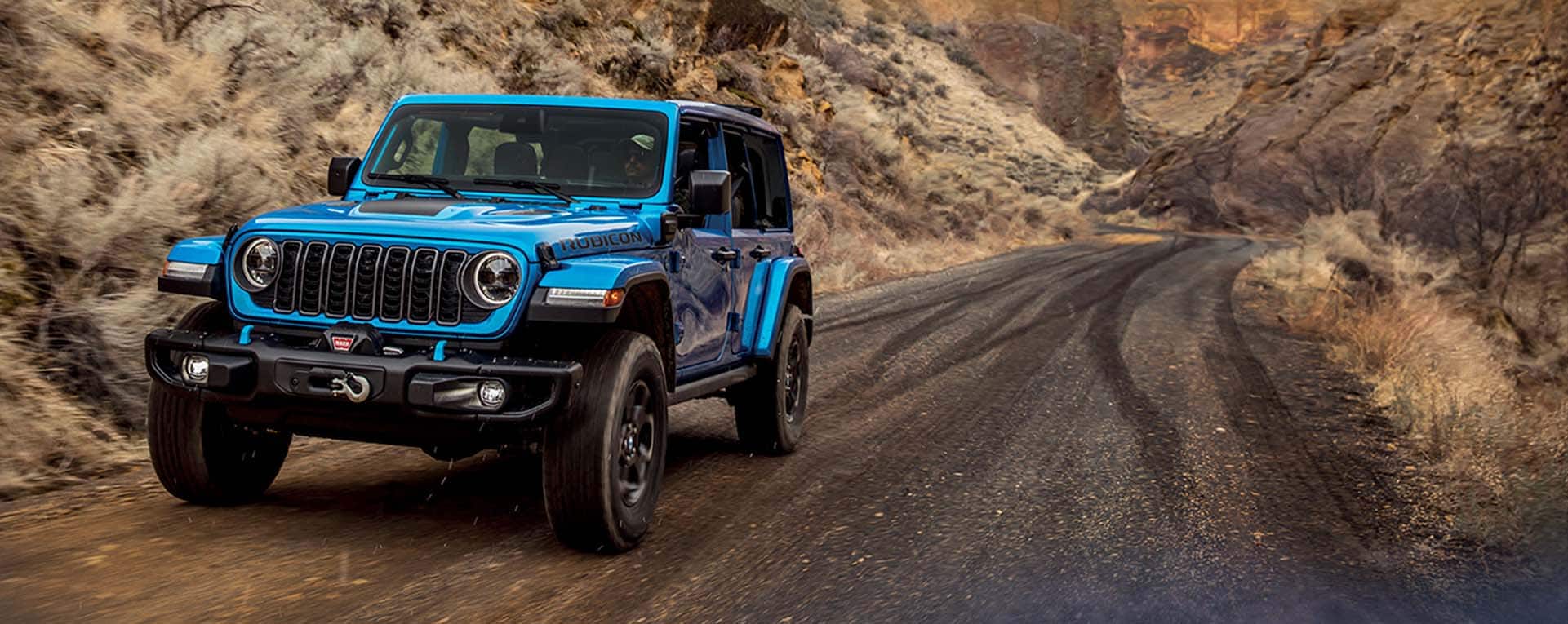Un Jeep Wrangler Rubicon 4xe 2024 azul circulando por un sendero que atraviesa las montañas.