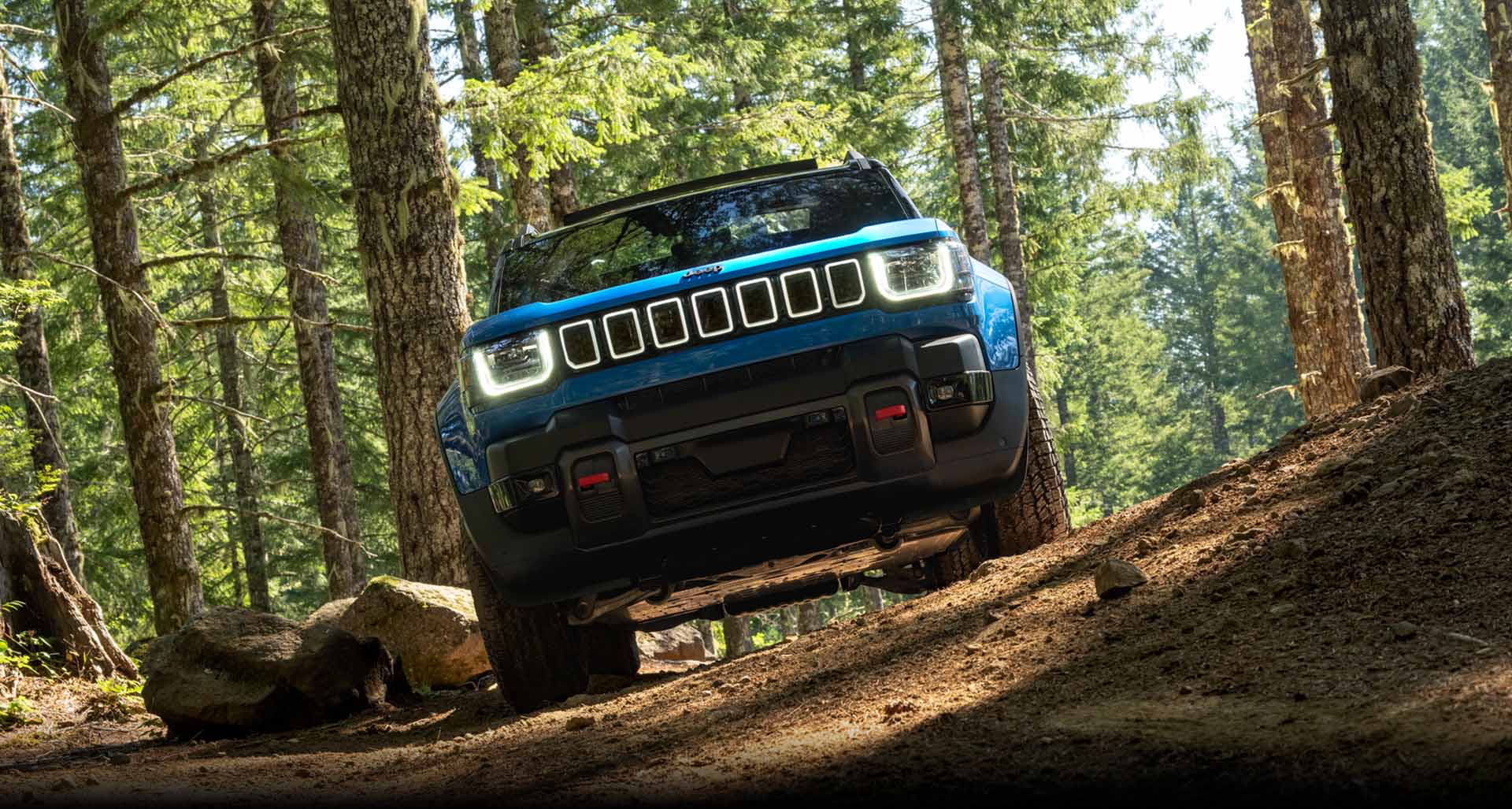 A blue 2026 Jeep Recon Moab, parked on a trail in the woods.