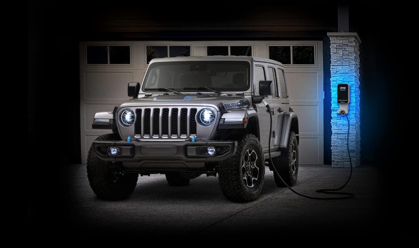 The 2022 Jeep Wrangler Rubicon 4xe parked in a residential driveway and plugged into a charging port beside the garage door.