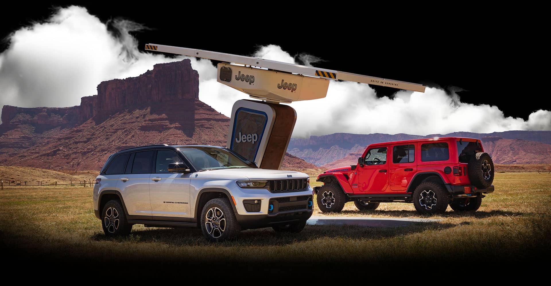 A 2022 Jeep Wrangler Rubicon 4xe and Jeep Grand Cherokee Trailhawk 4xe parked at a charging station surrounded by mountains.
