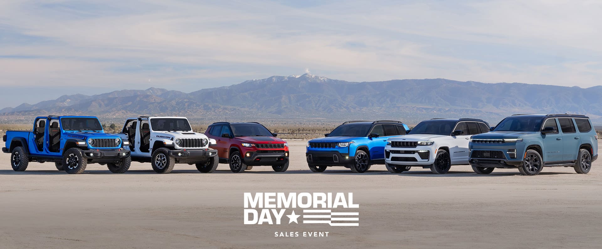 A lineup of six 2026 Jeep Brand vehicles parked in a semicircle. From left to right: a blue Gladiator Rubicon and white Wrangler Rubicon X—both with their doors and tops removed, a red Compass Trailhawk with black hood insert, a blue Cherokee Overland, a white Grand Cherokee Summit Obsidian, and a blue gray Grand Wagoneer Upland. Memorial Day Sales event.