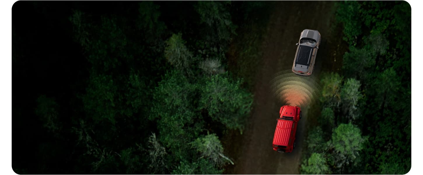 An overhead shot of a red Jeep Gladiator driving behind a gray Jeep Compass on a dark country road. Pixelated waves emit from the front of the Gladiator to illustrate the range of its Forward Collision Warning system.