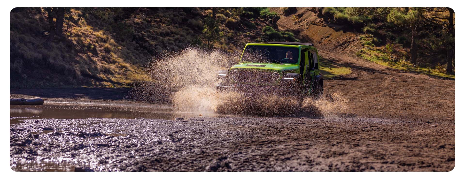 Un Jeep Wrangler Rubicon 2026 de cuatro puertas, color verde lima, vadeando un arroyo embarrado todoterreno, levantando una nube de polvo y agua a su paso.