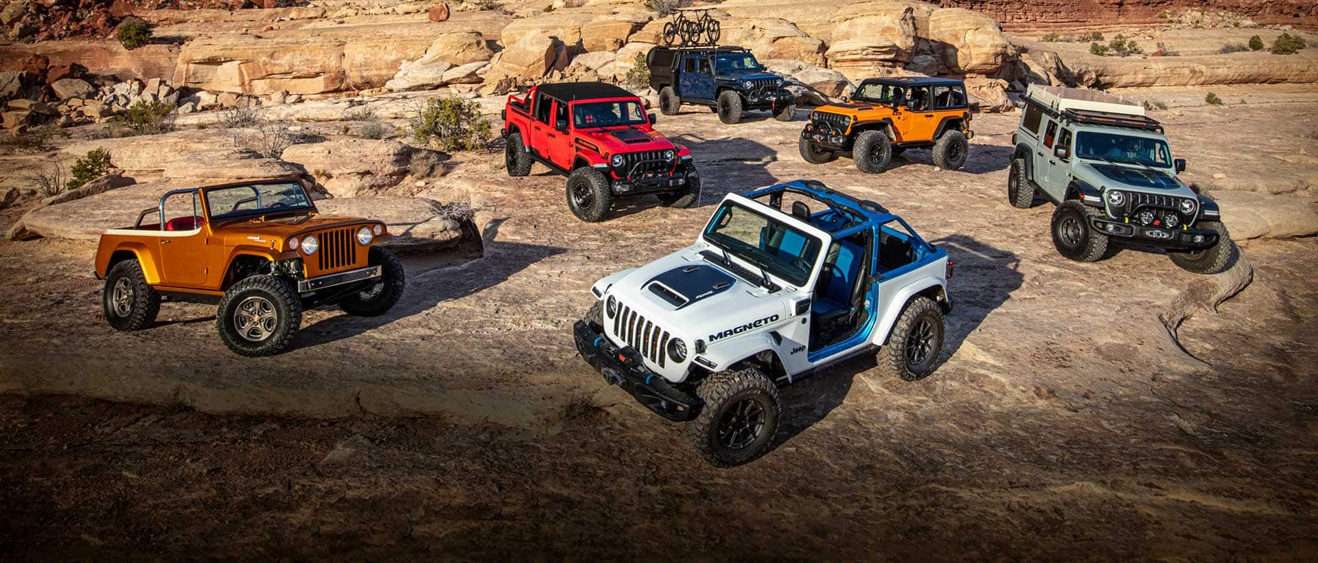 A set of six Jeep Brand Concept vehicles parked on a rocky plateau in the mountains.