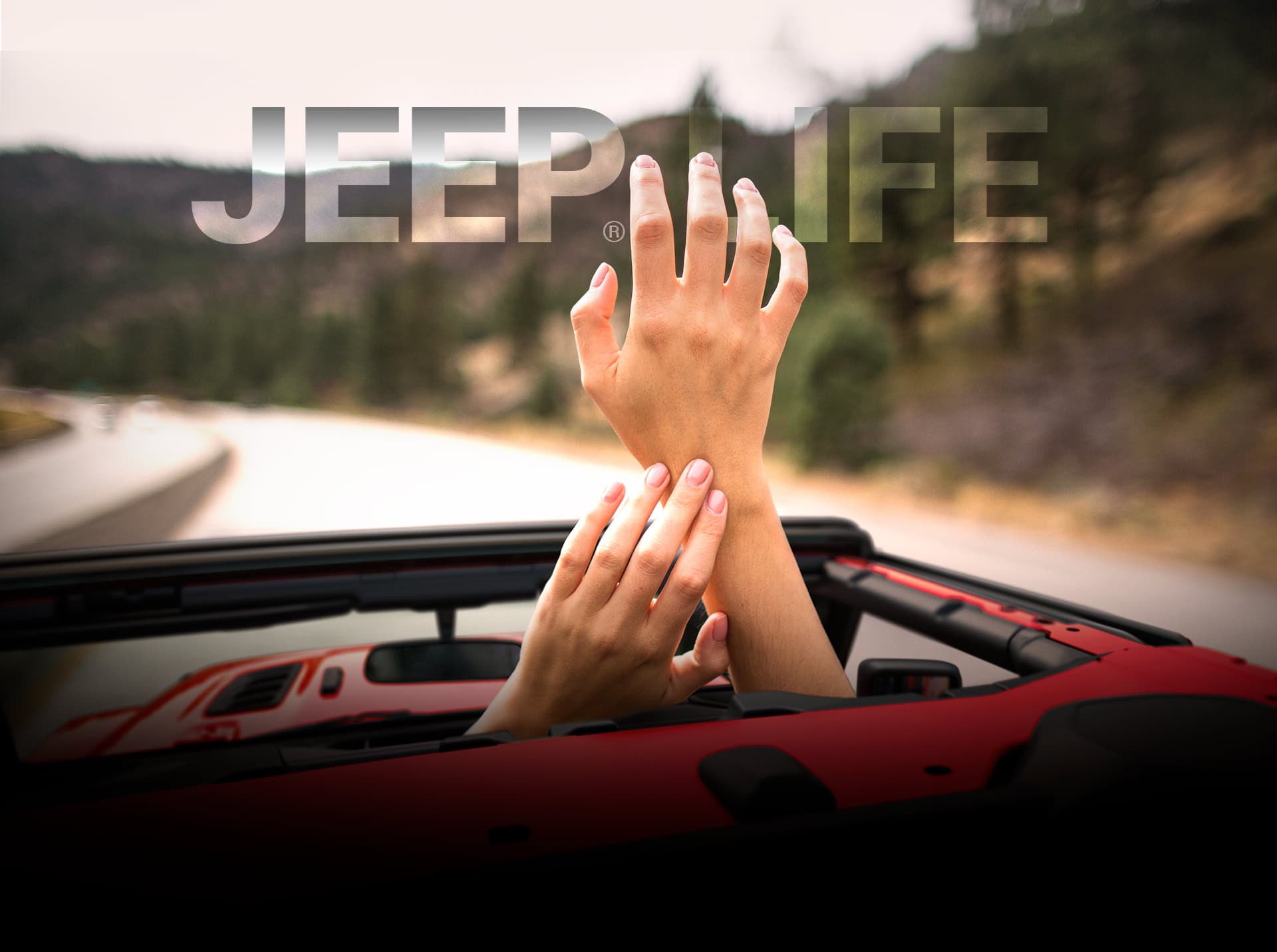 Vida Jeep. Un par de manos estirándose hacia el cielo a través del techo abierto de un Jeep Wrangler rojo.