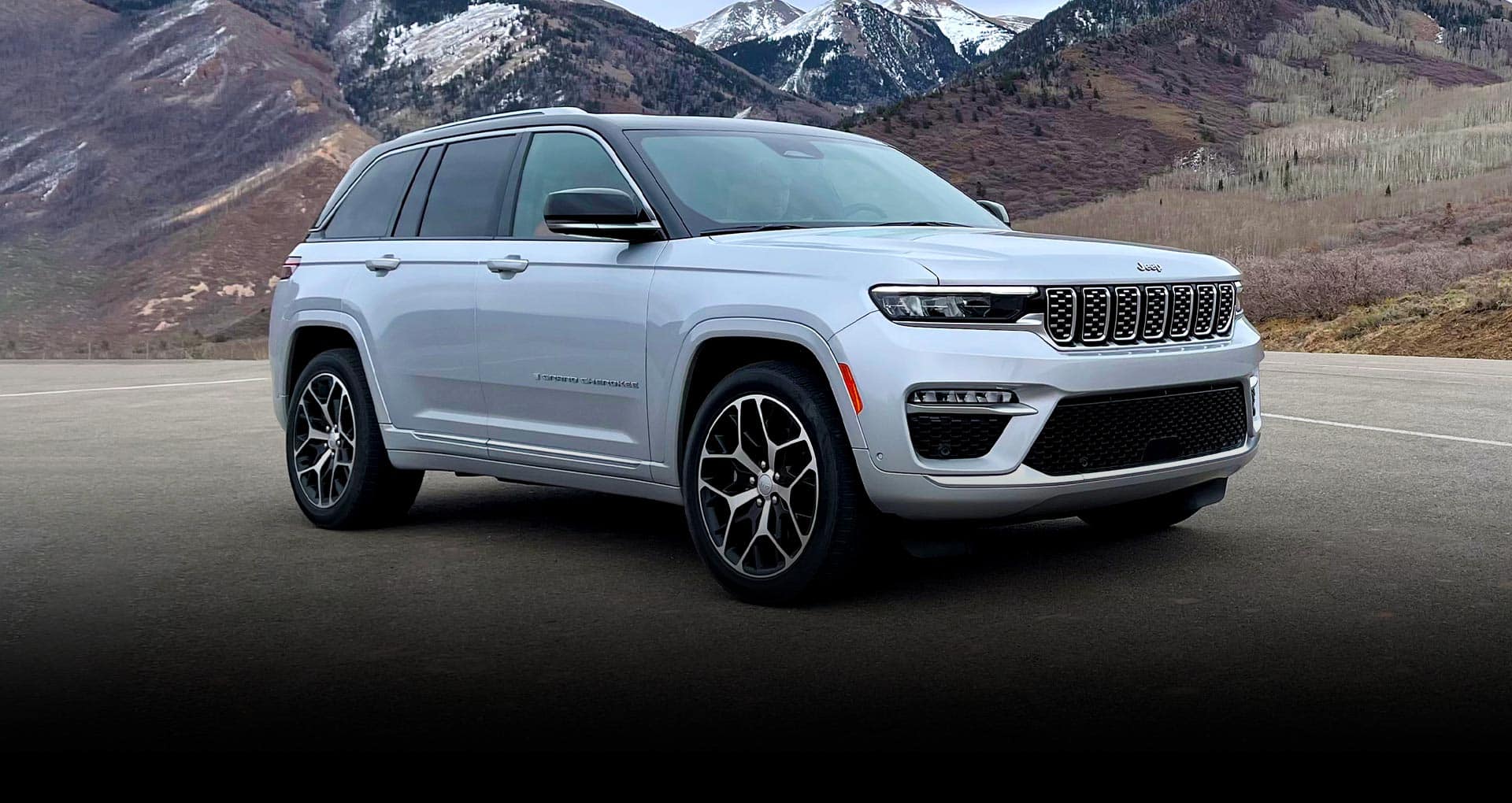 An angled profile of a white 2023 Jeep Grand Cherokee Summit Reserve with a mountain range in the background.