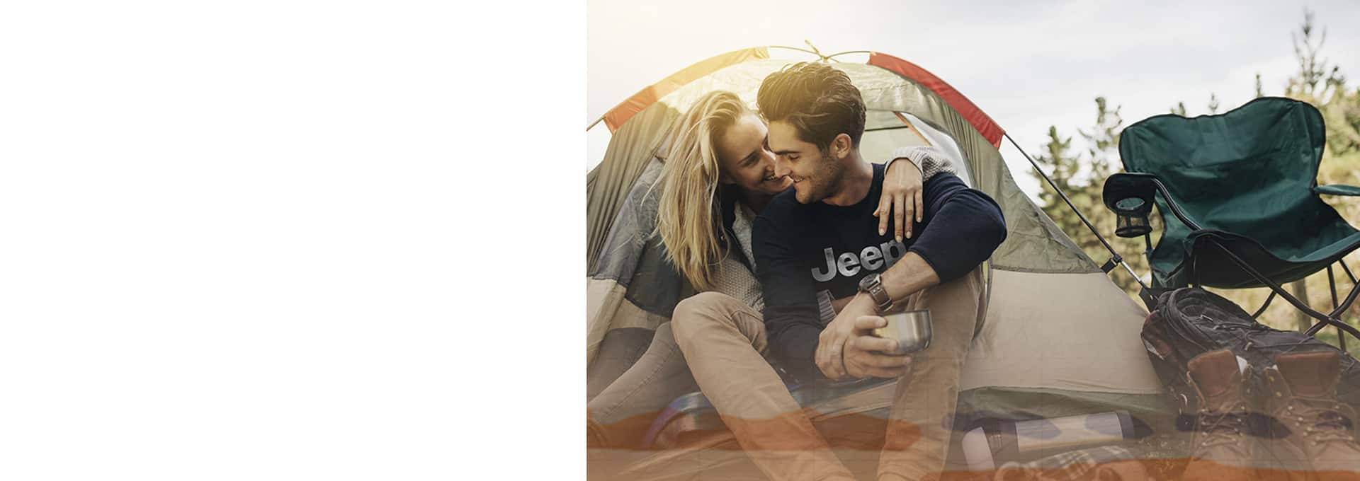 A couple sitting beside a tent and camping gear. The man is wearing a Jeep Brand sweatshirt.