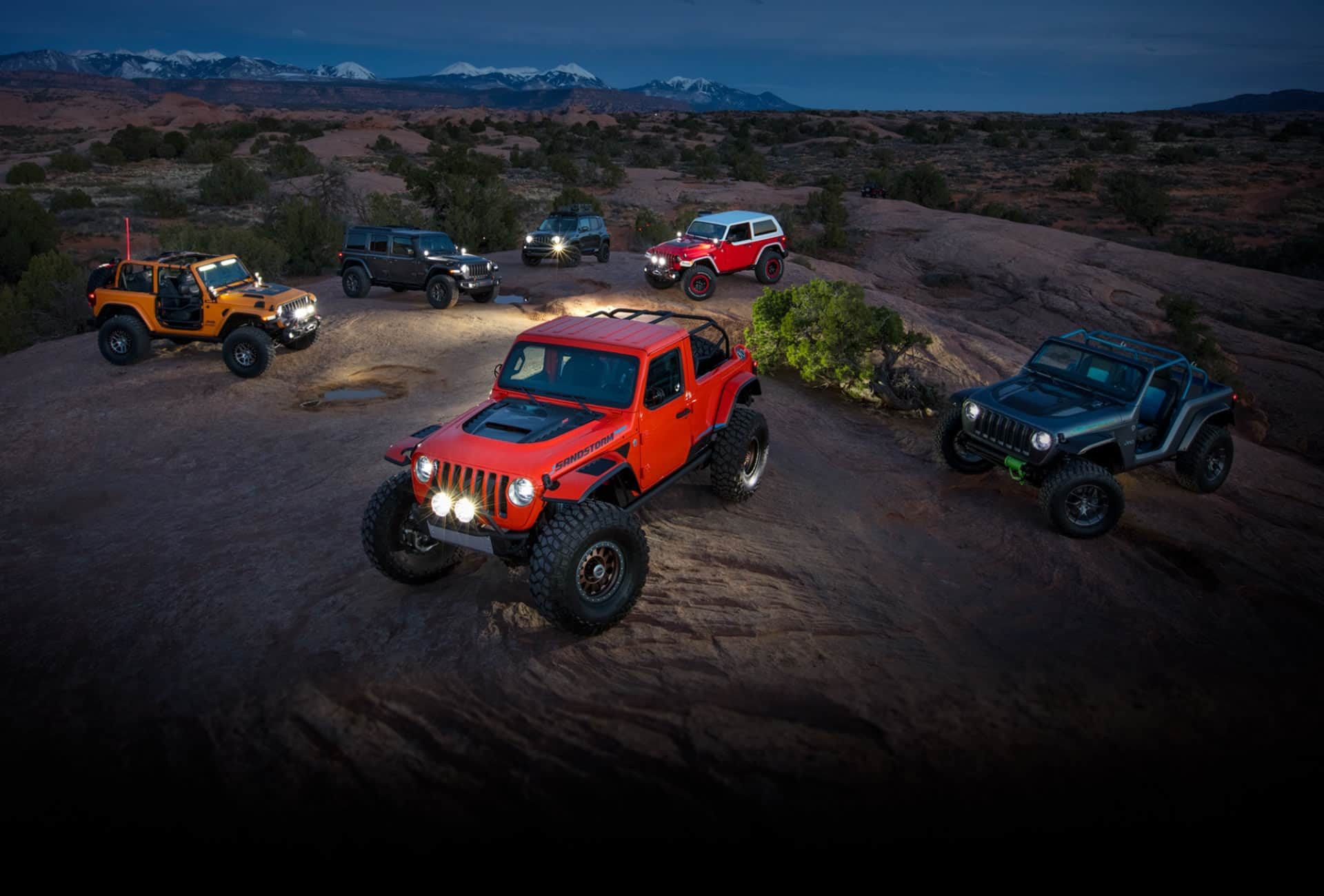 Grupo de seis vehículos conceptuales Jeep estacionados en una colina del desierto por la noche.