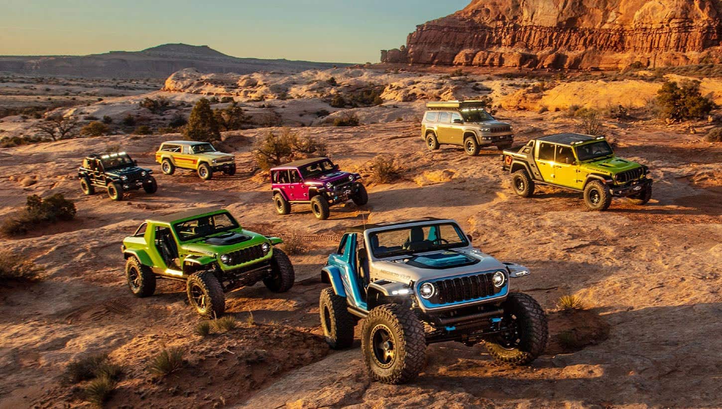 Un grupo de siete vehículos conceptuales de la marca Jeep estacionados de forma aleatoria en el desierto, sobre terreno irregular.