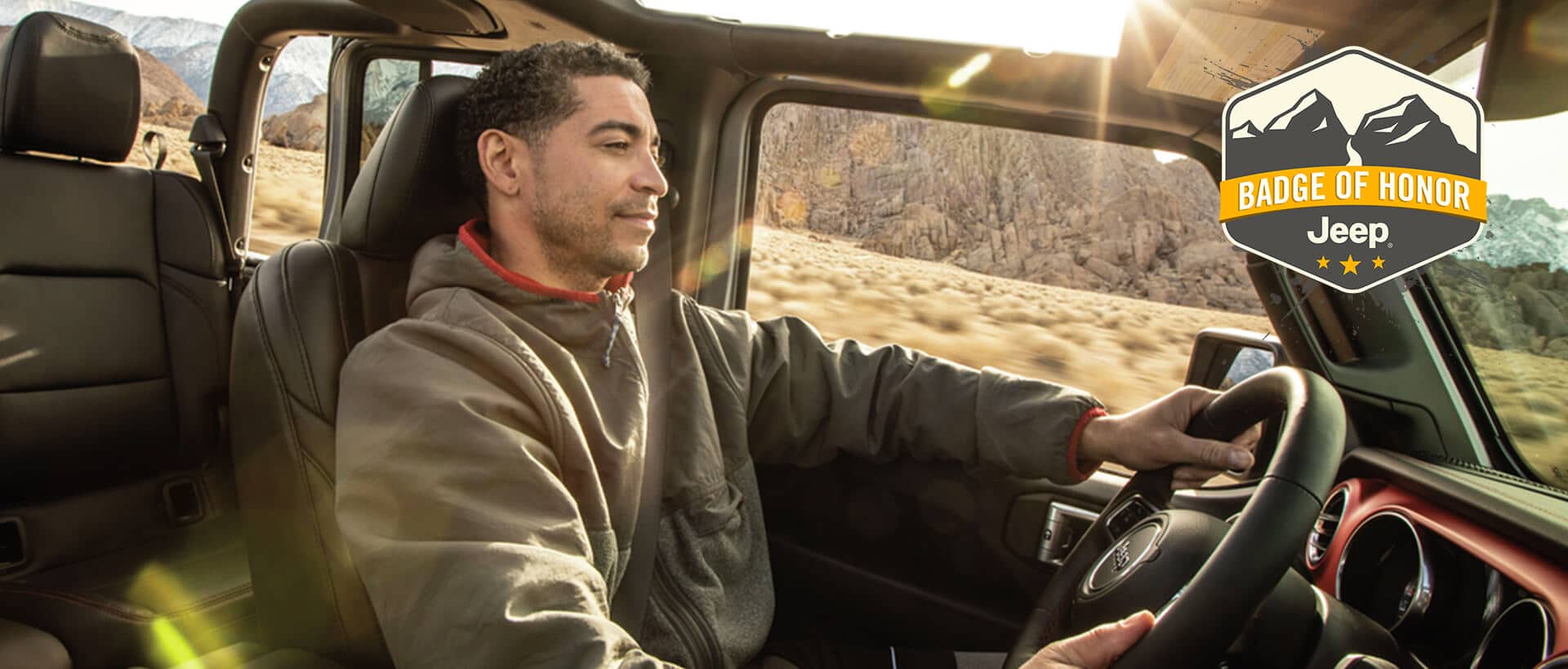 Un hombre manejando un Jeep Wrangler sin techo. Emblema de Honor de Jeep.
