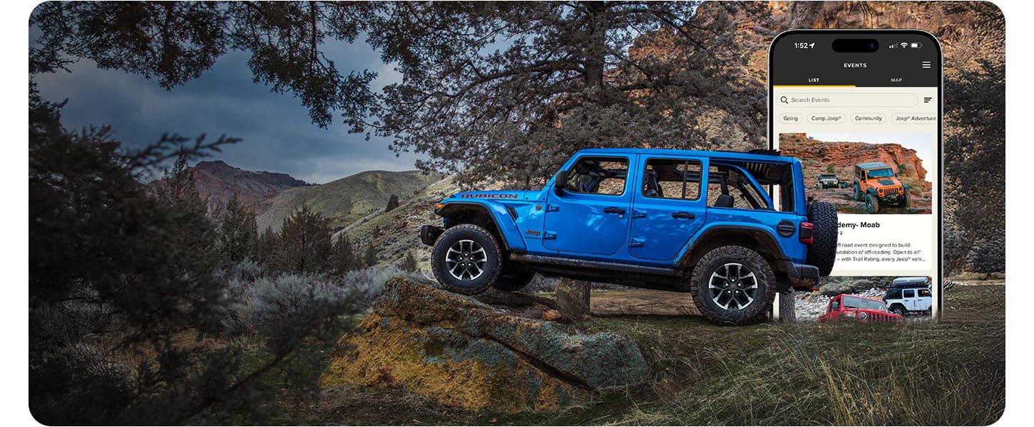 A driver-side profile of a blue 2026 Jeep Wrangler Rubicon X four-door, parked off-road, with its front tires elevated on a raised rock formation. In the background a smartphone screen displaying a Jeep app page.