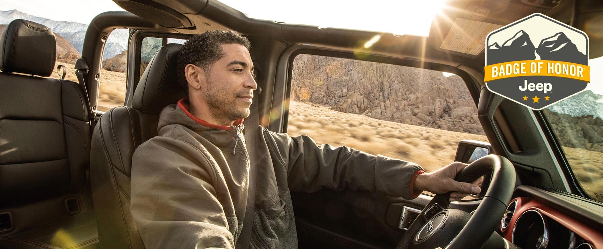 Un hombre manejando un Jeep Wrangler sin techo. Emblema de Honor de Jeep.