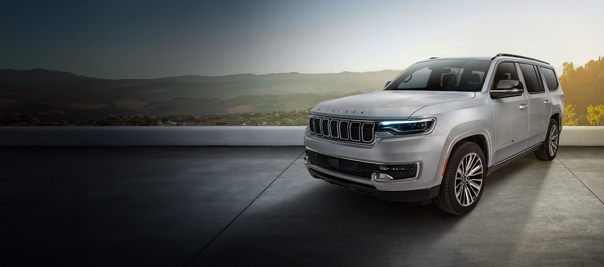 Ángulo delantero del lado del conductor de un Jeep Wagoneer Limited 2025 plateado con un valle y montañas de fondo.