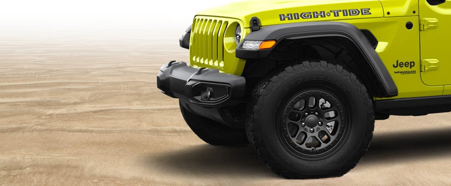 A close-up of the hood and front wheels of the 2022 Jeep Wrangler High Tide parked on sand.