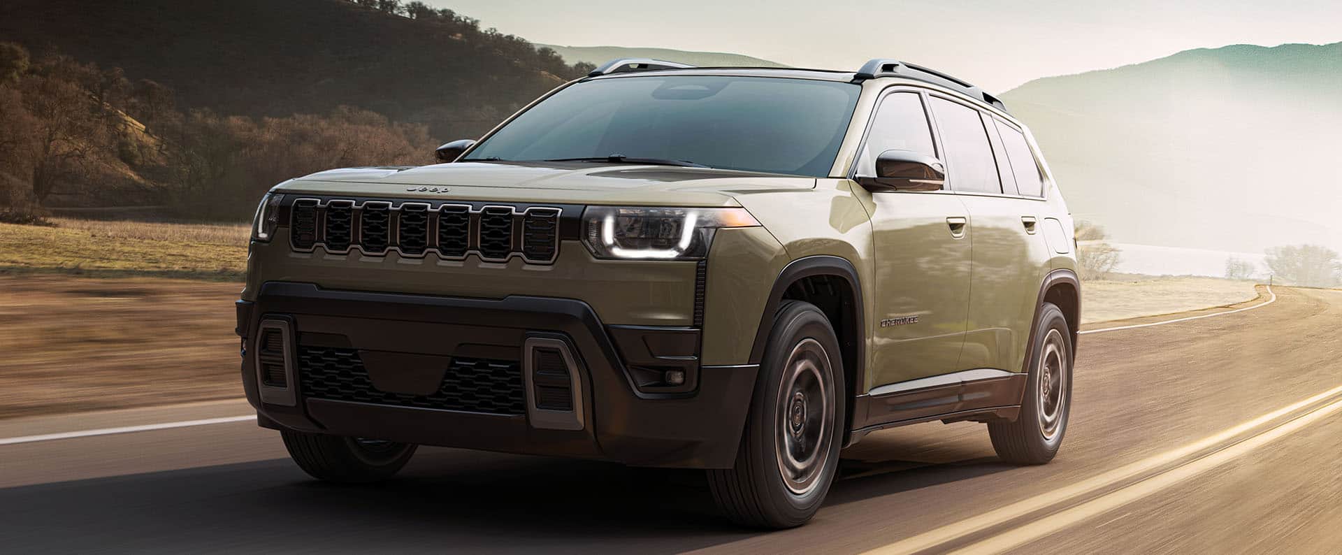 An olive green 2026 Jeep Cherokee Limited traveling down a curved highway.