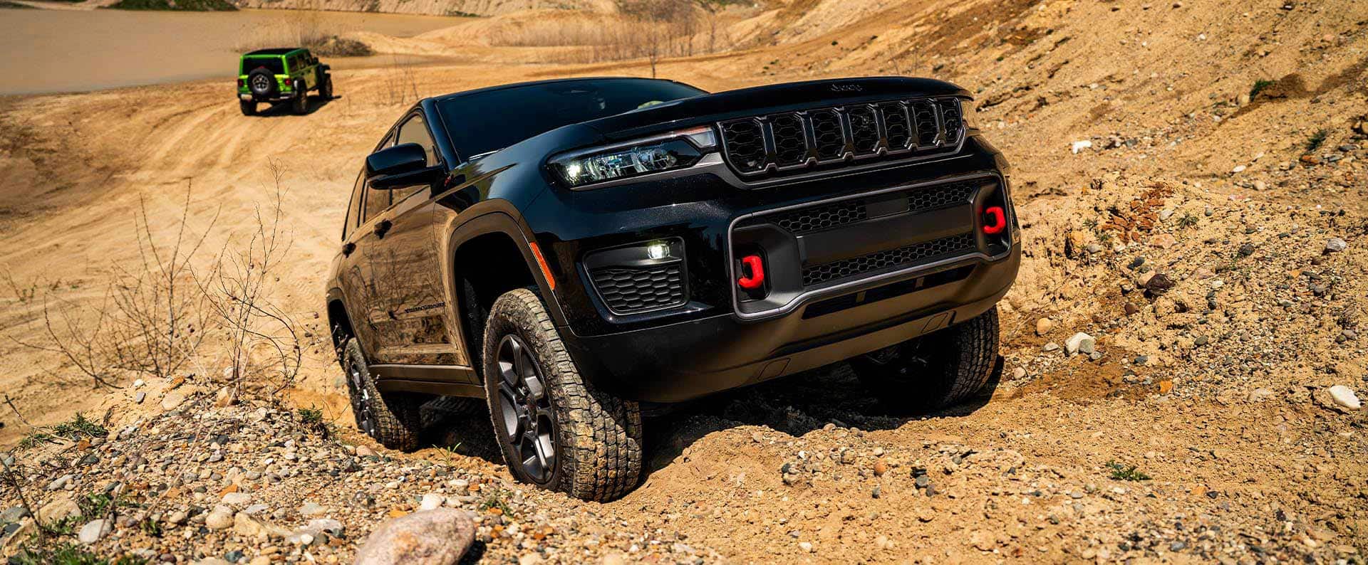 A black Jeep Cherokee with red tow hooks crawls up the rocky slope of a desert hill.