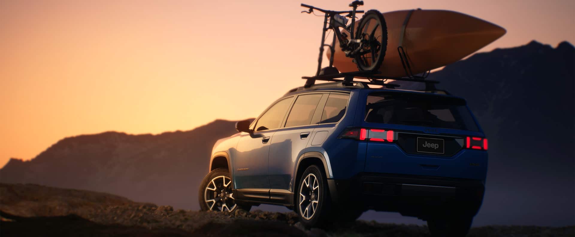 A blue 2026 Jeep Cherokee Overland with a kayak and part of a bike strapped to its roof rack, parked on a hill at sunset.