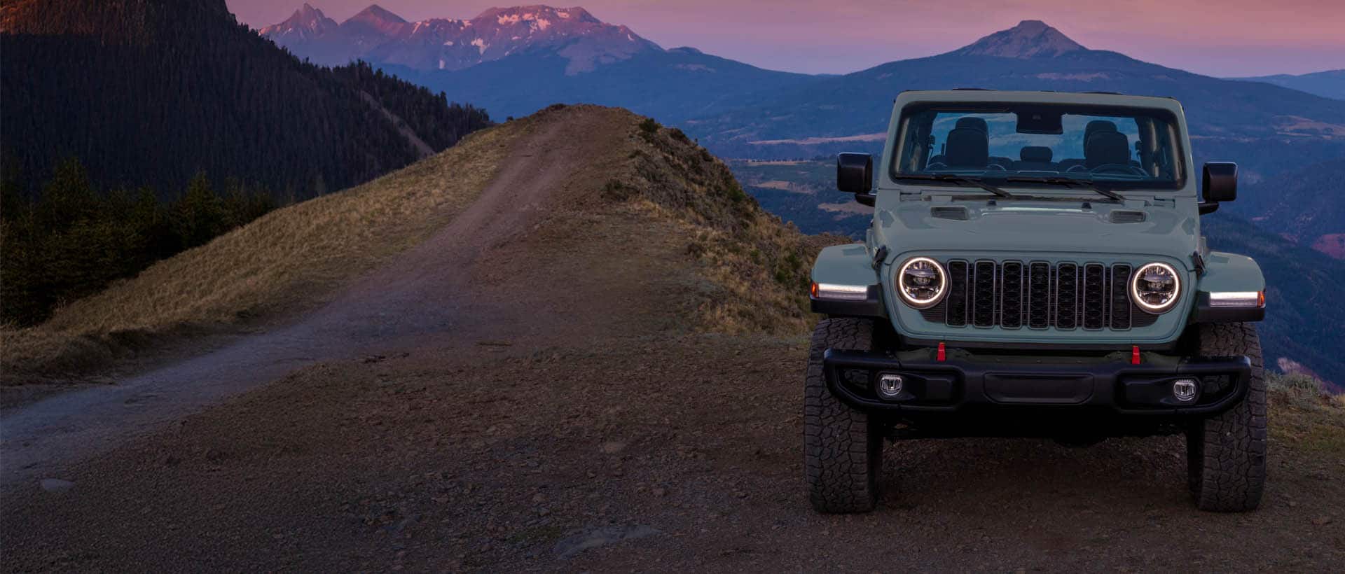 Un Jeep Wrangler Rubicon X 2025 gris azulado estacionado en un claro en las montañas, al atardecer.