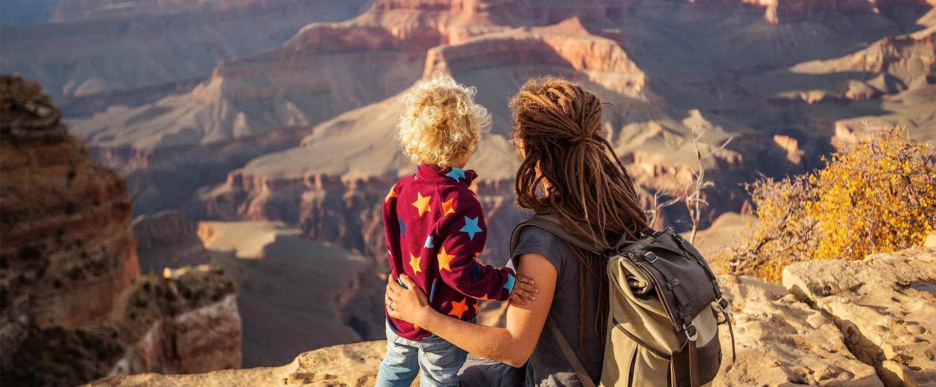 Una madre y un niño pequeño abrazados miran hacia un cañón inmenso.