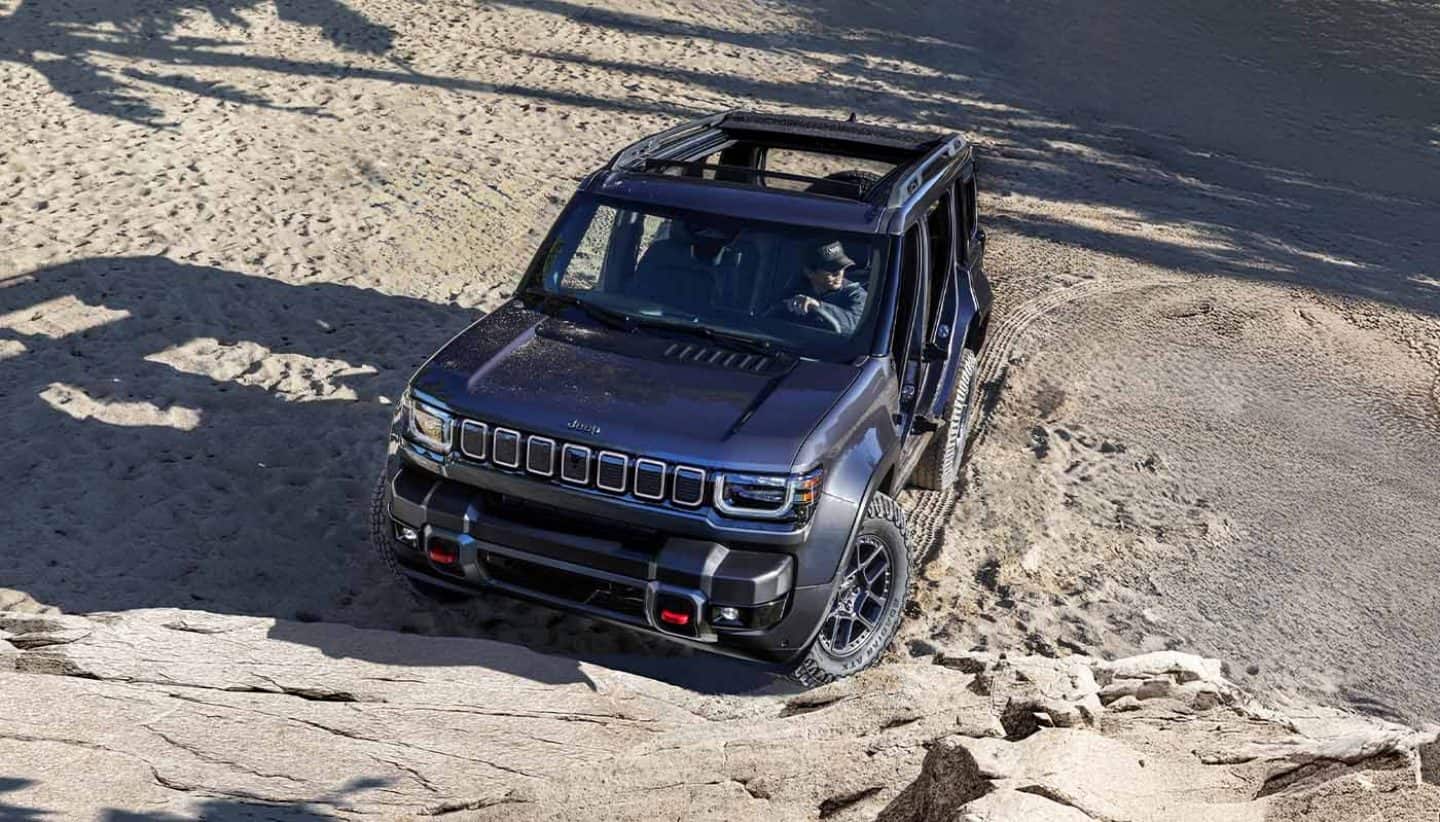 Display A raised angle of a 2026 Jeep Recon with its doors and top removed, about to scale a rocky hill off-road.