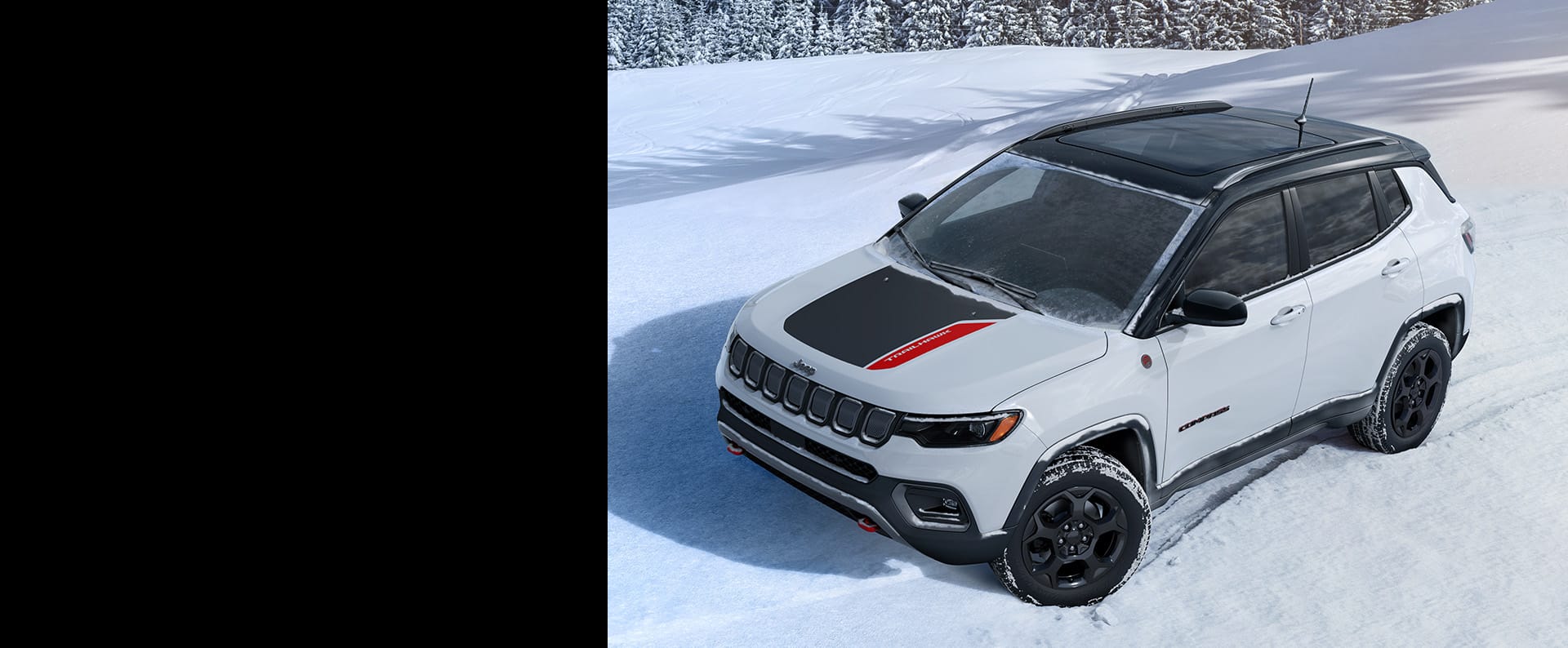 A 2023 Jeep Compass Trailhawk being driven on snow with a forest in the background.