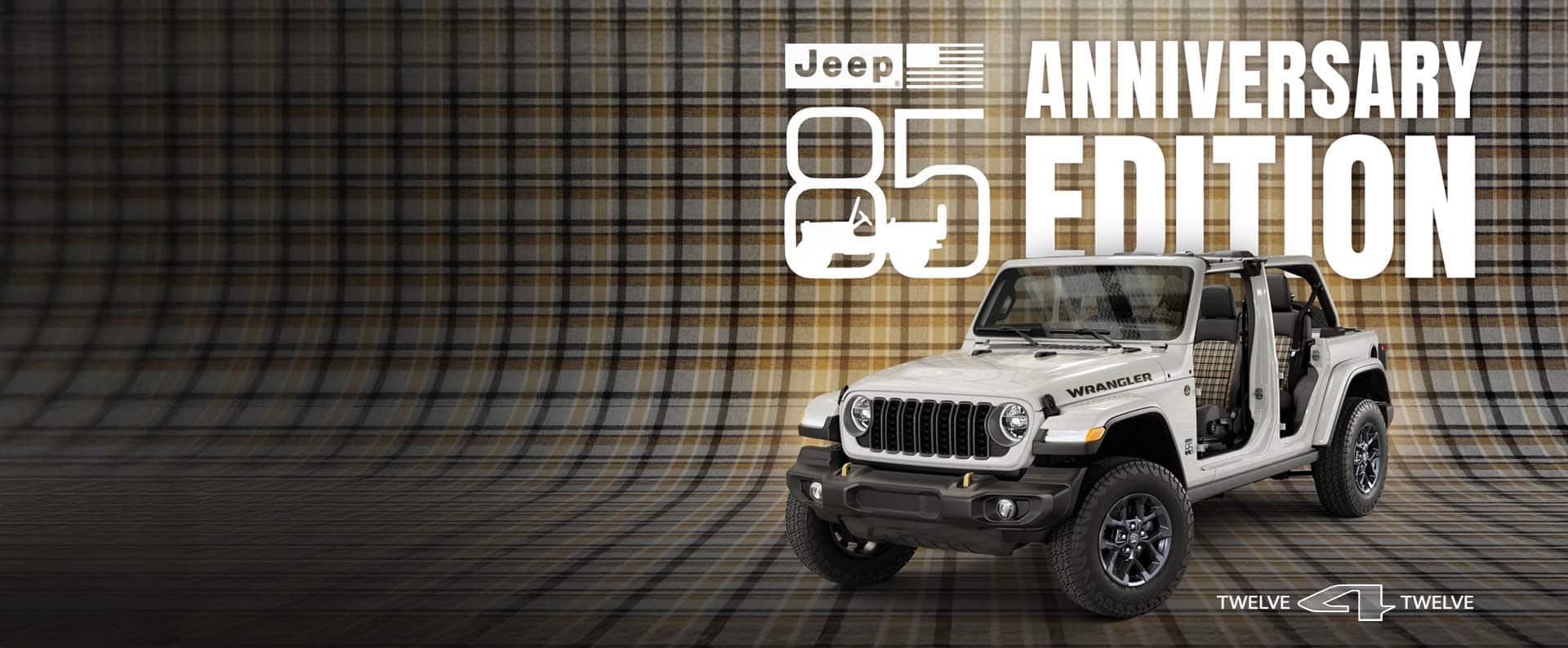A driver-side front angle of a white 2026 Jeep Wrangler 85th Anniversary Edition with its doors and top removed, revealing plaid inserts on the front and rear seats, parked on a seamless plaid surface that extends up the wall behind it. Jeep 85 Anniversary Edition.