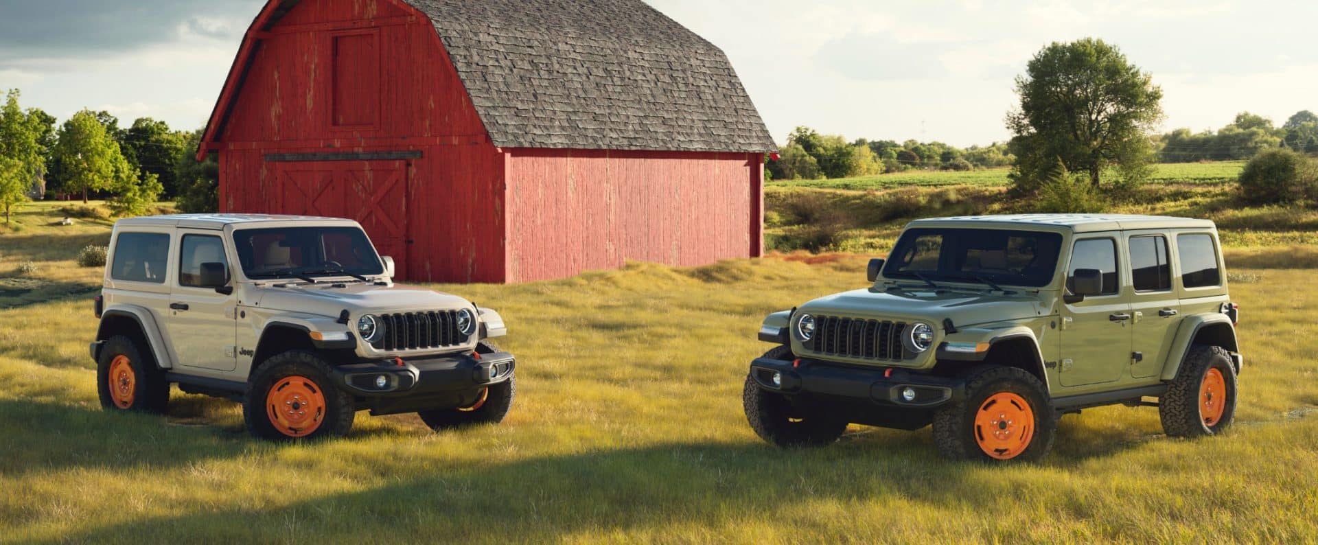 Tan and green 2027 Jeep Wrangler JL-2A models sitting in a grassy field with a red barn in the background.