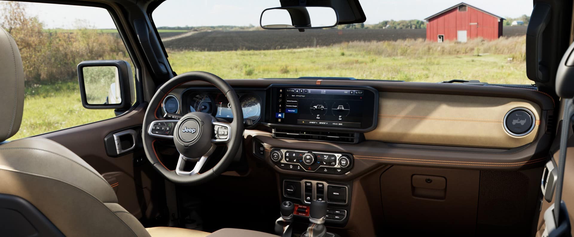An interior shot of the front dashboard of the 2027 Jeep Wrangler JL-2A, with a grassy field and a red barn showing through the windshield.