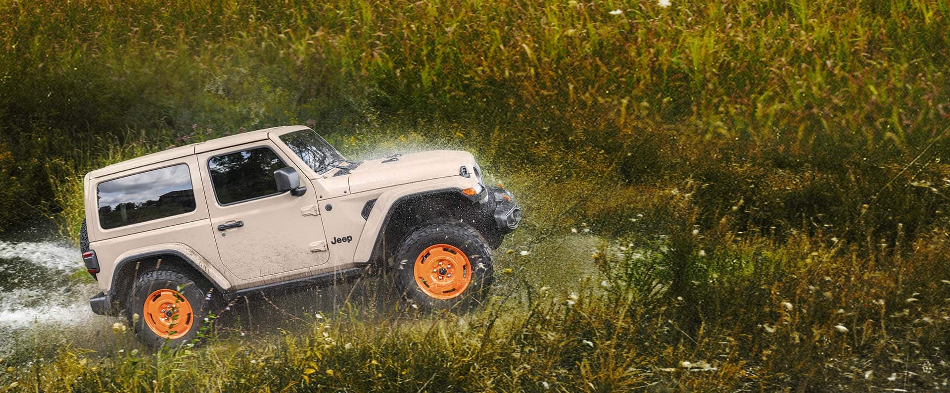 A 2027 Jeep Wrangler JL-2A drives out of a creek onto a grassy field.