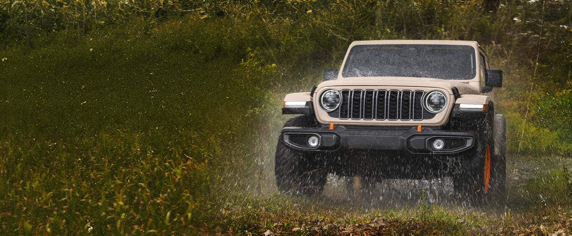 A 2027 Jeep Wrangler JL-2A drives through a grassy field, kicking up water as it goes.
