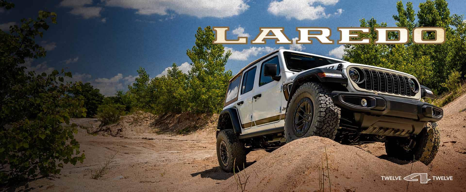 A white 2027 Jeep Wrangler Laredo crawling over a boulder on a desert trail off-road. Laredo. 12 for 12.