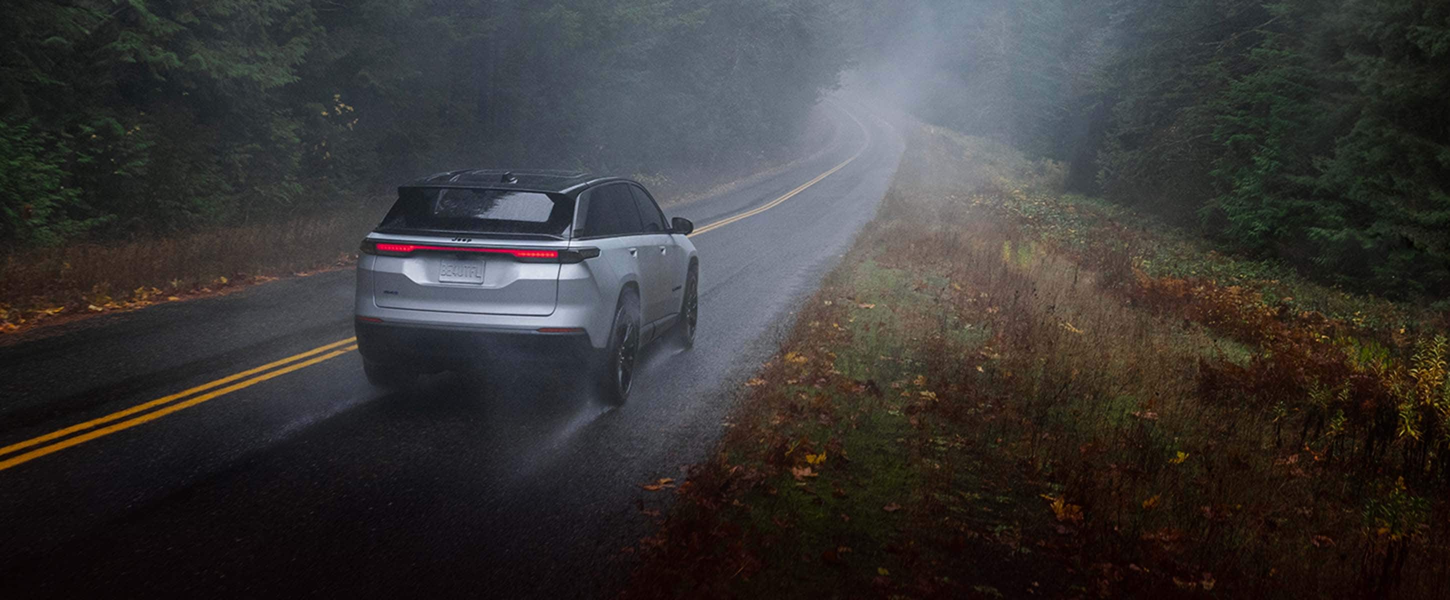 Un Jeep Wagoneer S Launch Edition 2024 blanco viajando bajo una tormenta por una carretera en el bosque.