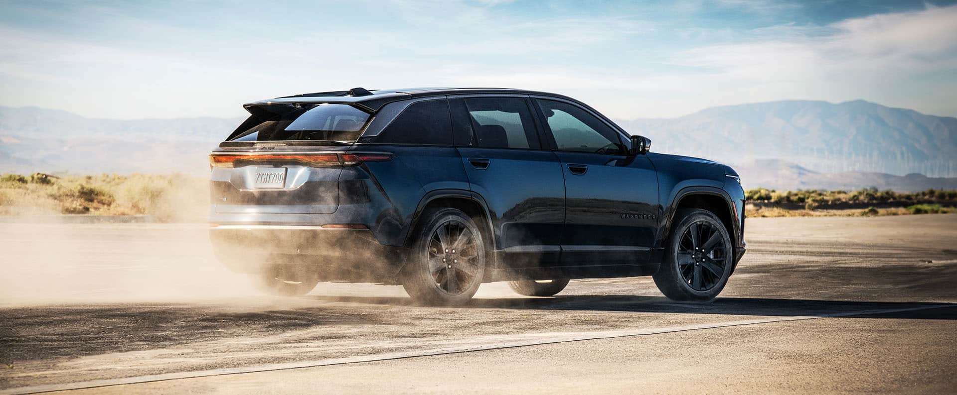 A passenger-side rear angle of a 2024 Jeep Wagoneer S Launch Edition being driven on a desert road, kicking up dust as it goes.