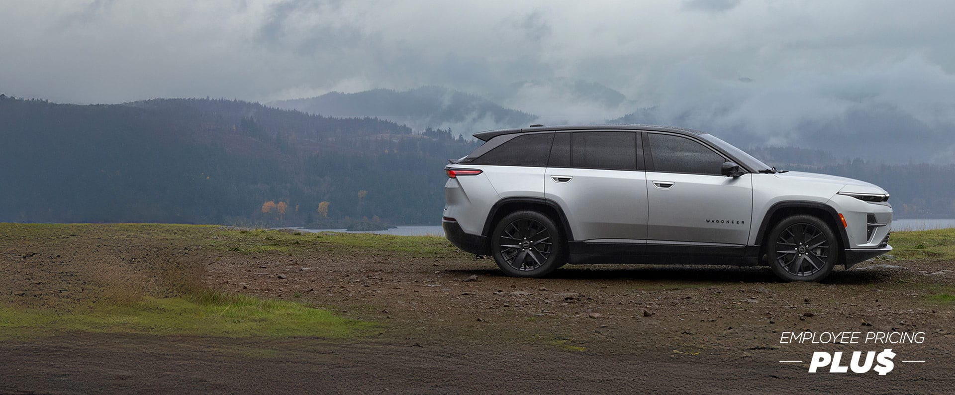 A passenger-side profile of a silver 2024 Jeep Wagoneer S Launch Edition, parked near a body of water with a overcast sky and fog in the distance. Employee Pricing Plus.