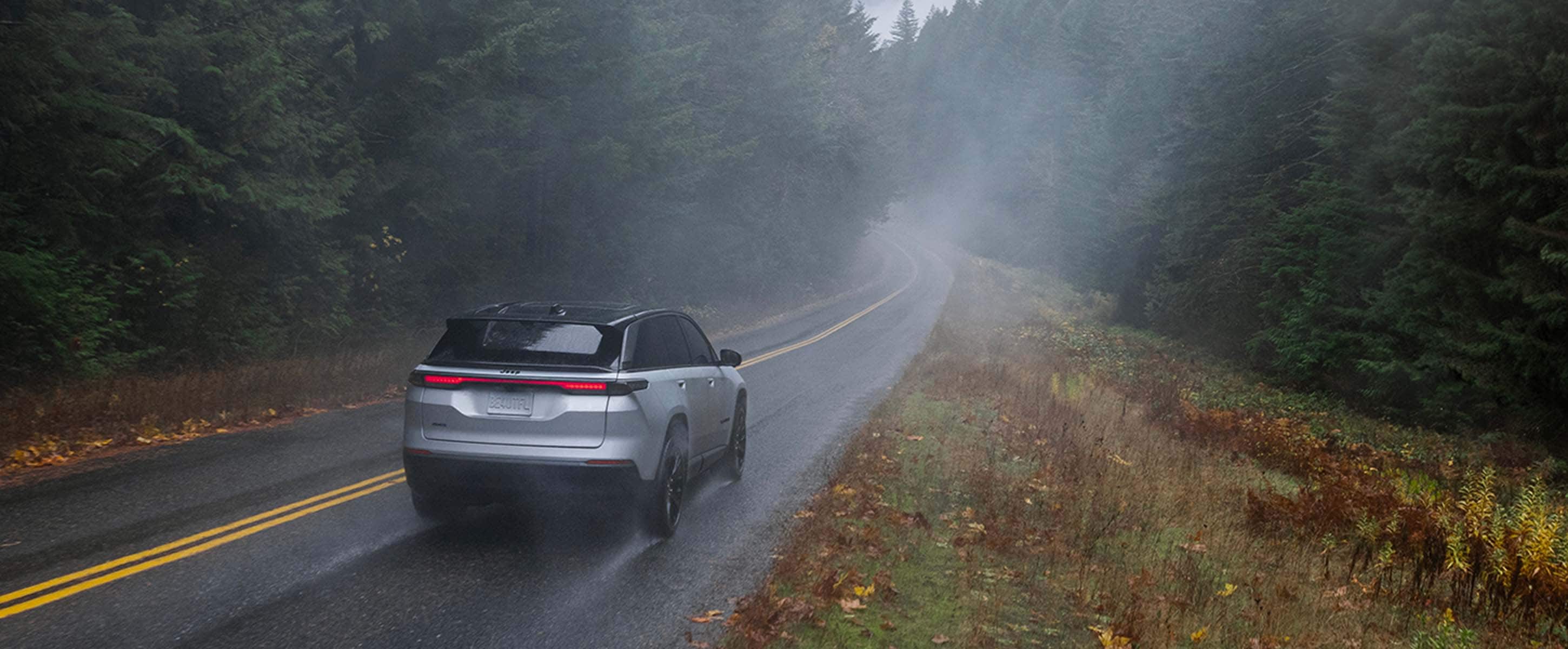 A white 2024 Jeep Wagoneer S Launch Edition traveling in a rainstorm on a highway in the woods.
