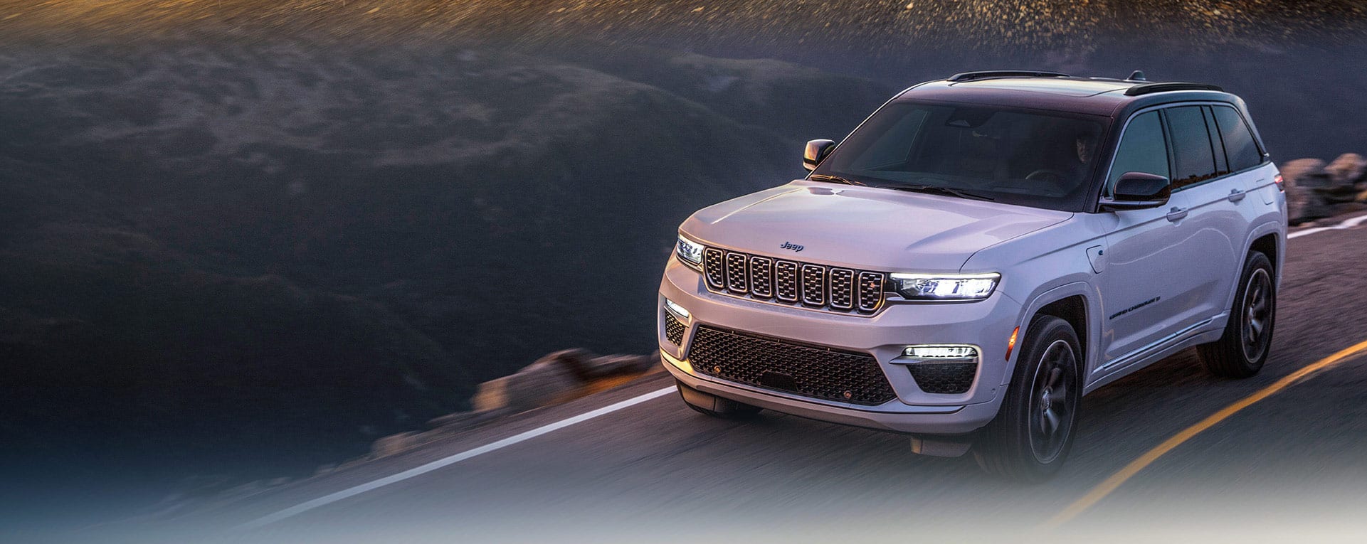 A white 2024 Jeep Grand Cherokee Trailhawk 4xe with a black hood insert, being driven off-road.