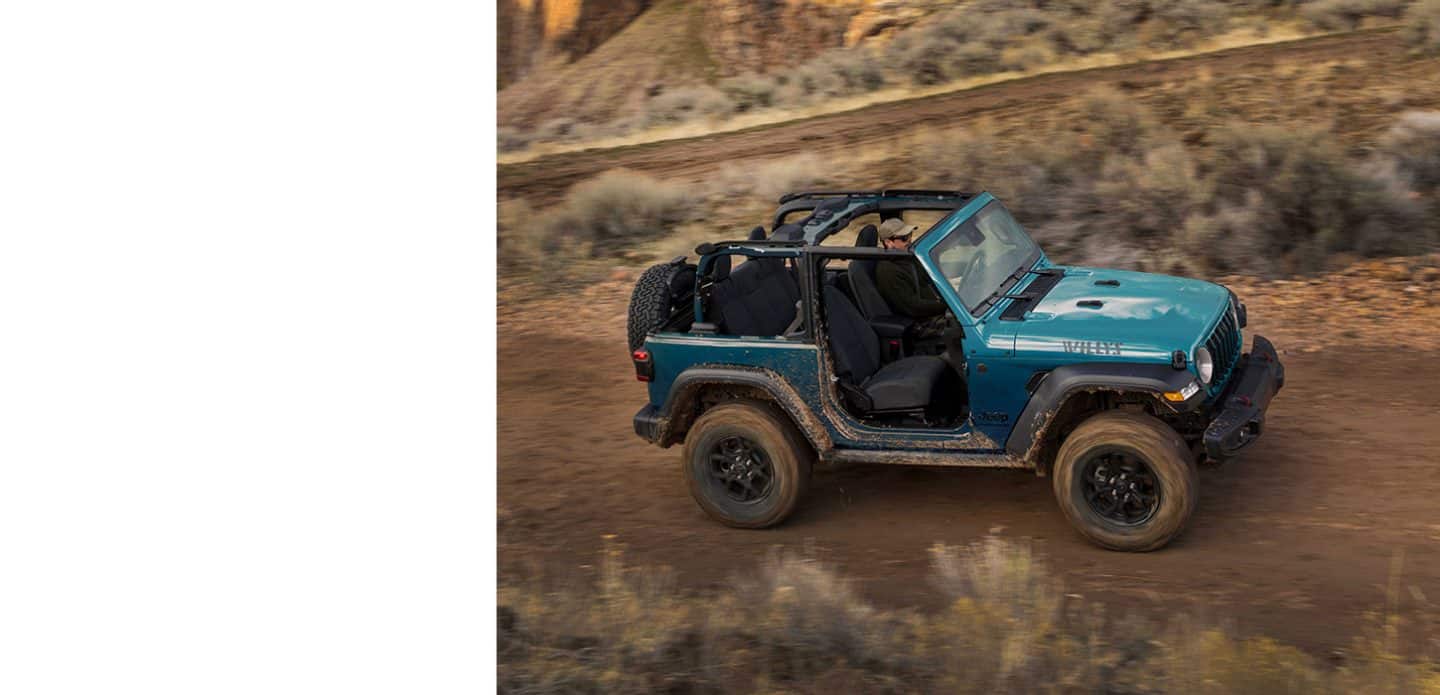 A blue 2025 Jeep Wrangler Willys with its doors and roof removed, traveling on a trail, off-road.