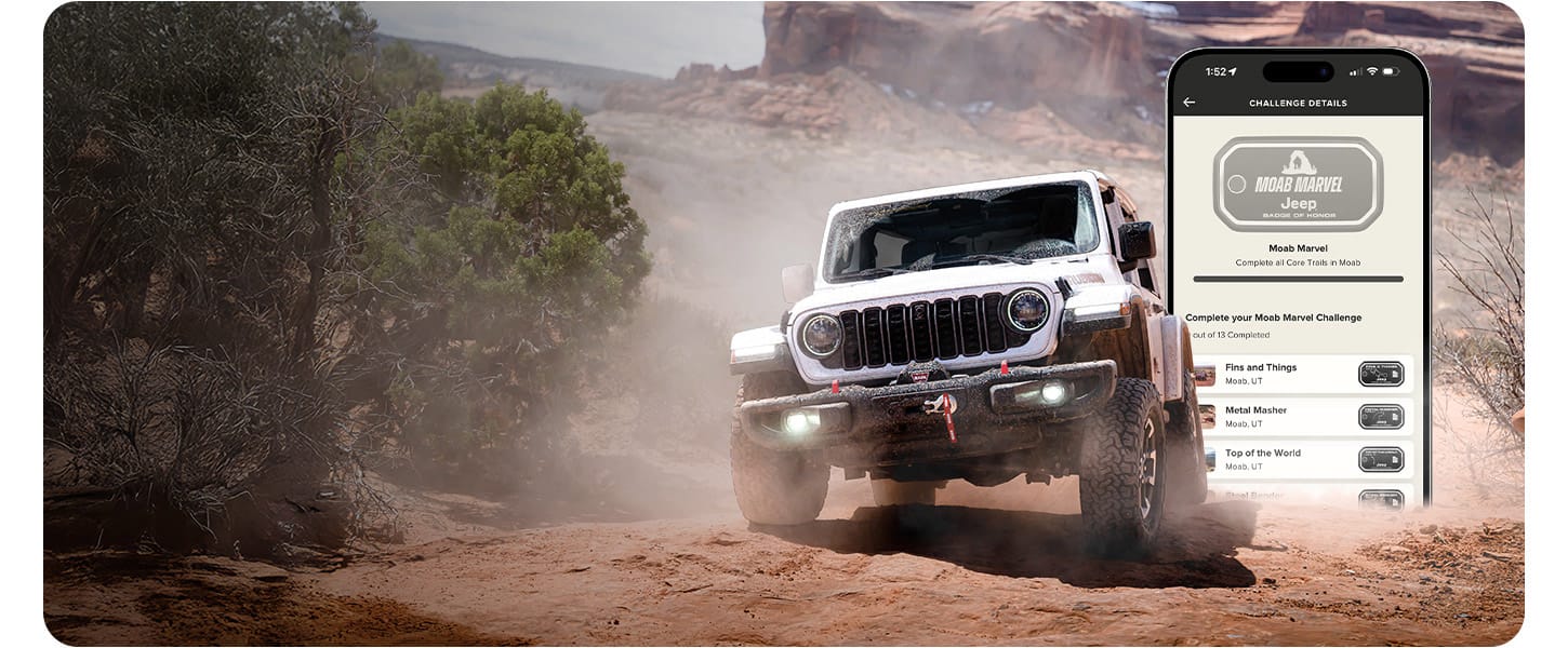 A head-on angle of a white 2026 Jeep Wrangler Rubicon X four-door, crawling over a rocky trail. In the background a smartphone screen displaying a Jeep trail challenge.