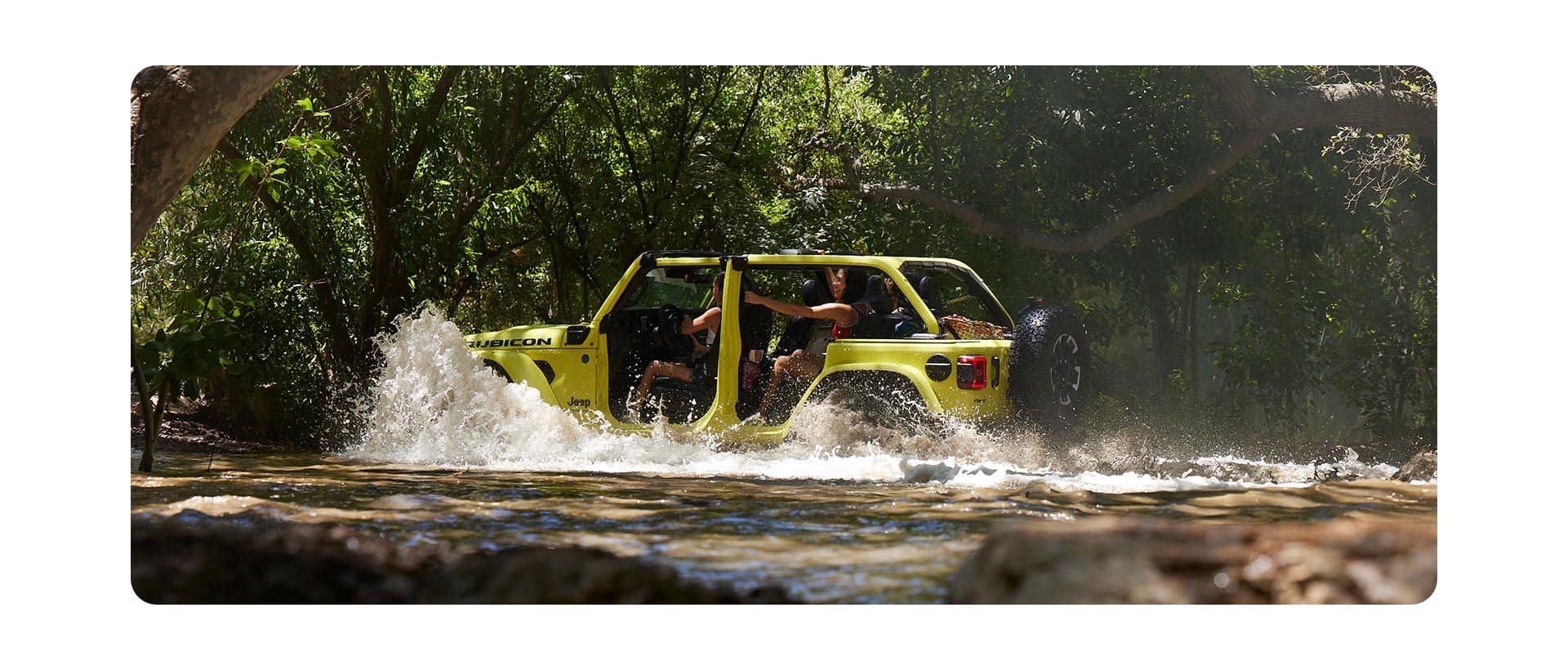 A yellow 2024 Jeep Wrangler Rubicon X with its doors and roof removed, fording through a deep stream with water splashing above its wheel wells.